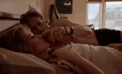 a man and a woman are laying in bed holding hands and touching noses .
