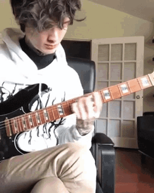 a man is sitting in a chair playing an electric guitar .