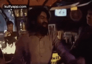 a man with a beard is standing in a room with his hands outstretched .