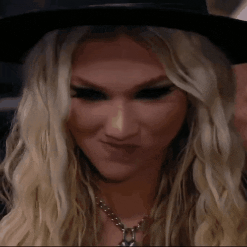 a blonde woman wearing a black hat and necklace