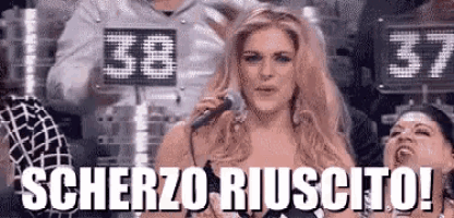 a woman is singing into a microphone while holding a sign that says scherzo riuscito .