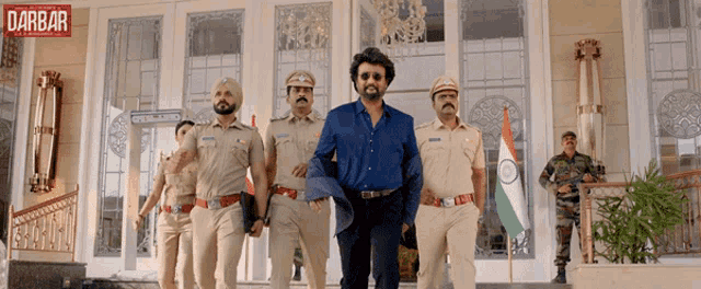 a group of police officers walking in front of a building with the word darbar on the bottom right