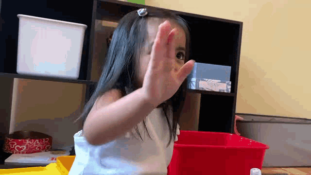 a little girl making a stop sign with her hand in front of a red bin