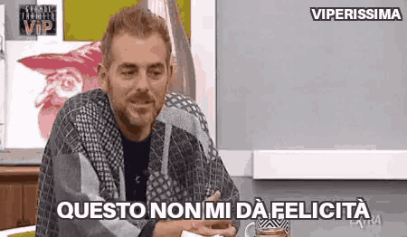 a man with a beard is sitting at a table with a cup of coffee and a sign that says viperissima .