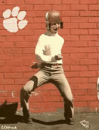 a man is dancing in front of a brick wall that has a clemson logo on it