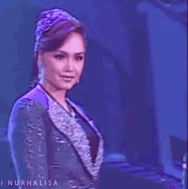 a woman in a purple dress is dancing on a stage in front of a purple background .