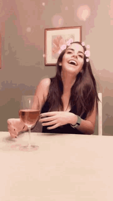 a woman is sitting at a table holding a glass of wine and laughing