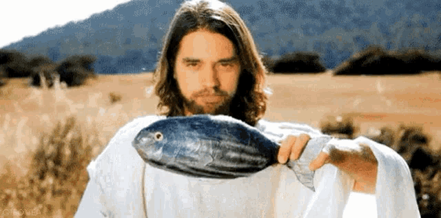 a man in a white robe is holding a large fish in his hand .