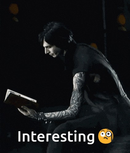 a man with tattoos is reading a book in the dark