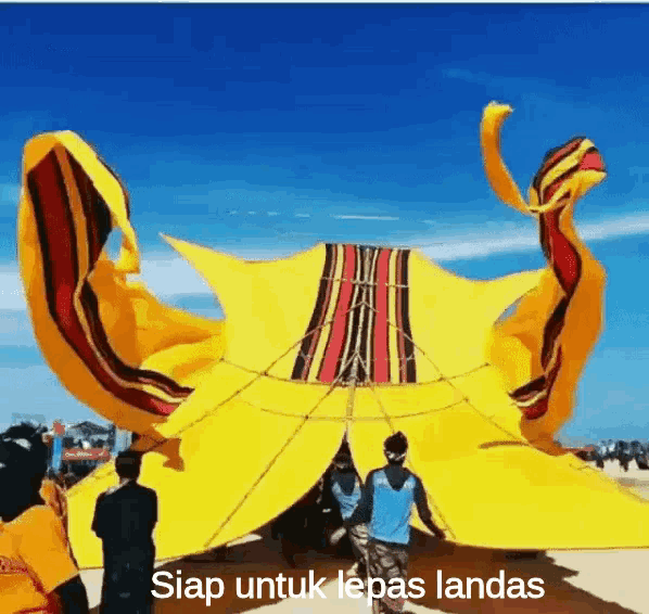a group of people are standing around a large yellow kite with the words siap untuk lepas landas below it