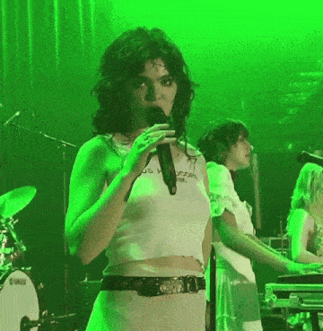 a woman singing into a microphone in front of a green background