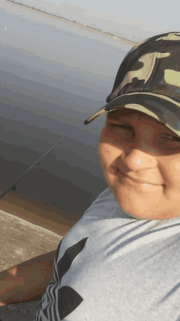 a boy wearing a camo hat is holding a fishing rod and smiling