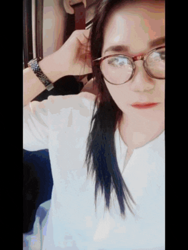 a woman wearing glasses and a white shirt is taking a selfie