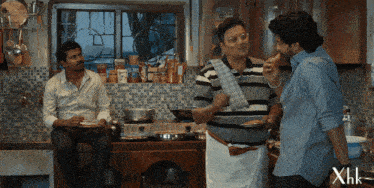 three men in a kitchen with xhk written on the bottom right corner