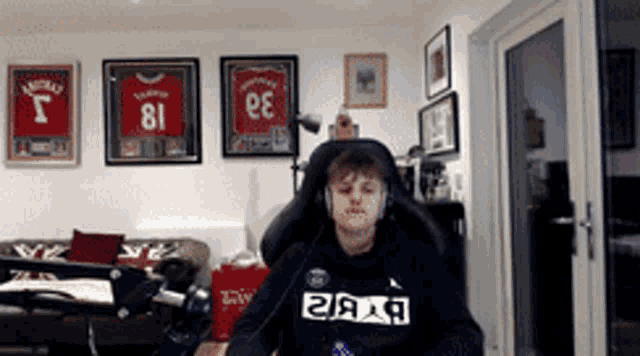 a man wearing headphones is sitting in a chair in front of framed jerseys including one with the number 81