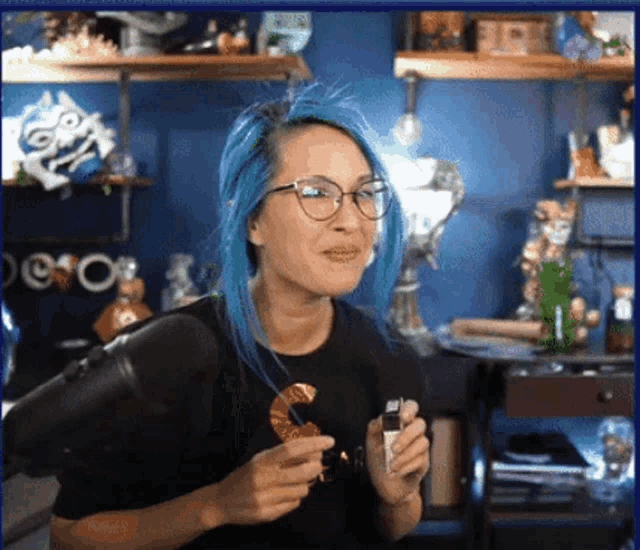 a woman with blue hair is wearing glasses and a black shirt with the letter s on it