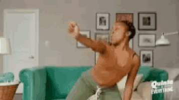a shirtless man is dancing in a living room next to a couch .