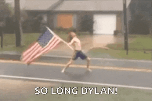 a shirtless man is running down a street holding an american flag .