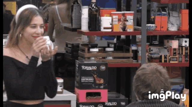 a woman drinking from a cup in front of a tobaldo espresso machine