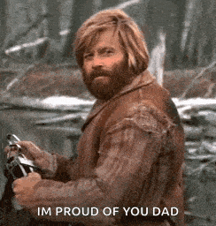 a man with a beard and long hair is holding a gun and says `` im proud of you dad '' .