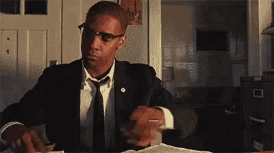 a man in a suit and tie is sitting at a desk with a book and a pen in his hand .