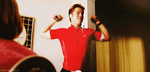 a man in a red shirt flexes his muscles while a woman watches