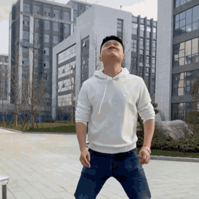 a man in a white hoodie stands in front of a building with his eyes closed