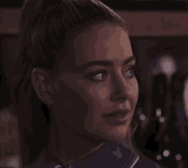 a close up of a woman 's face with a ponytail and a blue shirt