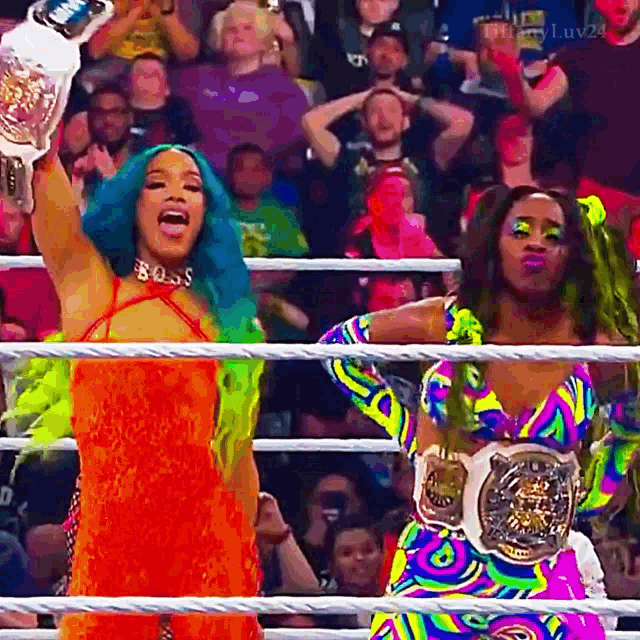 two women are standing in a wrestling ring holding up their championship belts .