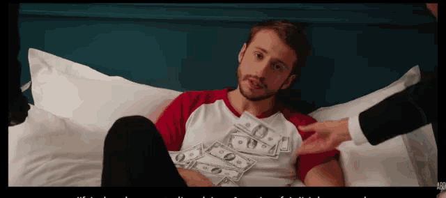 a man laying on a bed with a stack of money on his t-shirt