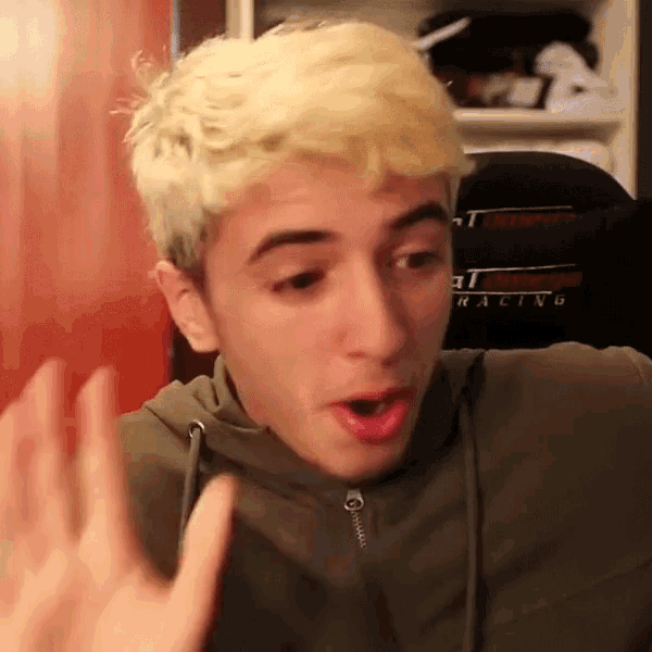 a young man with blonde hair is making a funny face while wearing a racing seat .