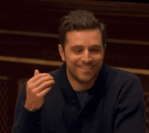 a man wearing a blue sweater is smiling and making a funny face