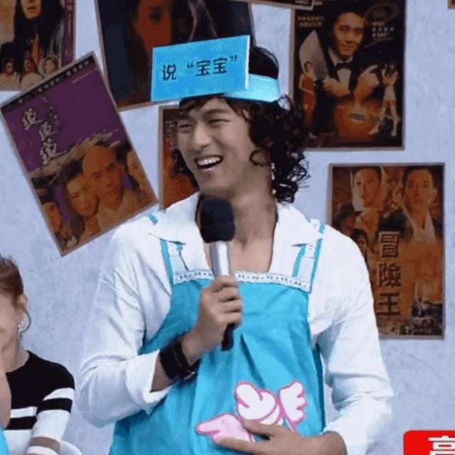 a man in a blue apron is holding a microphone and wearing a sign on his head that says " baby "