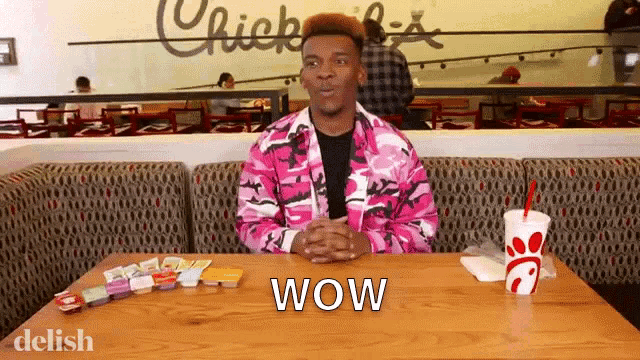a man in a pink jacket is sitting at a table in front of a chick-fil-a sign that says wow