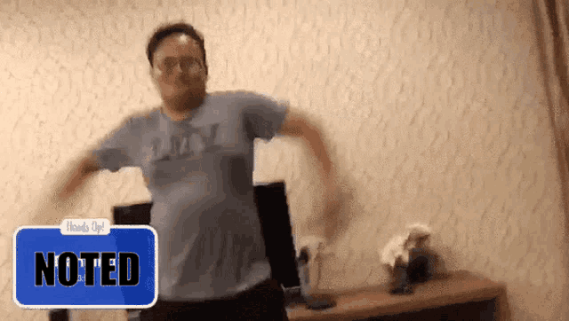 a man in a blue shirt is dancing in a room with a note that says noted on it