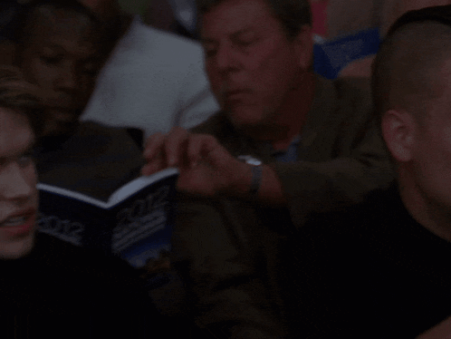 a man in a black shirt and red tie is reading a book called " poetry "