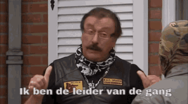 a man in a leather vest is talking to another man with the words ik ben de leider van de gang on the bottom