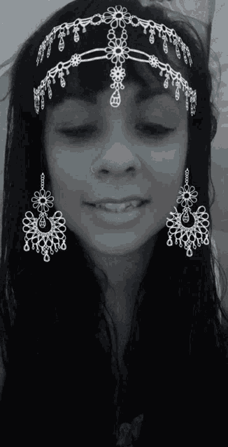 a black and white photo of a woman wearing a crown and earrings