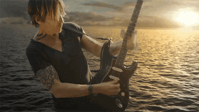 a man with a tattoo on his arm is playing a guitar in the water