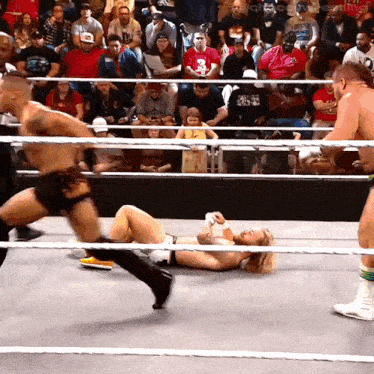 a wrestler is laying on the ground while another wrestler is running around