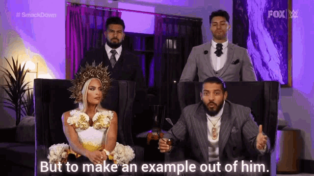 a man in a suit is sitting next to a woman in a white dress and a woman in a crown .