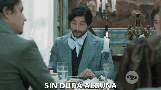 a man in a suit sits at a table with sin duda alguna written on the bottom