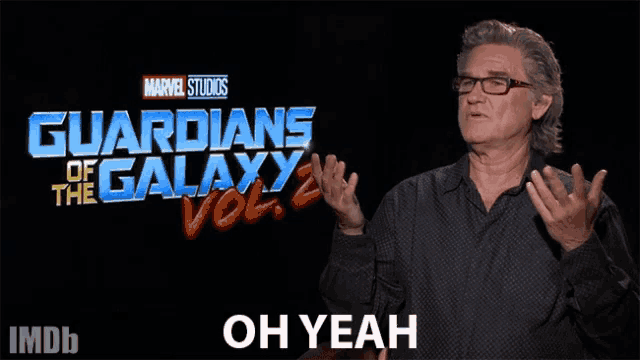 a man with glasses stands in front of a guardians of the galaxy logo