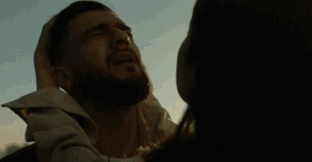 a man with a beard is crying while a woman holds his head in her hands .