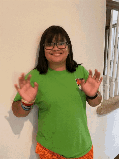 a girl wearing glasses and a green shirt is standing in front of a wall