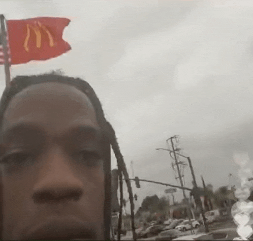 a man with dreadlocks is taking a selfie with a mcdonald 's flag flying in the background .