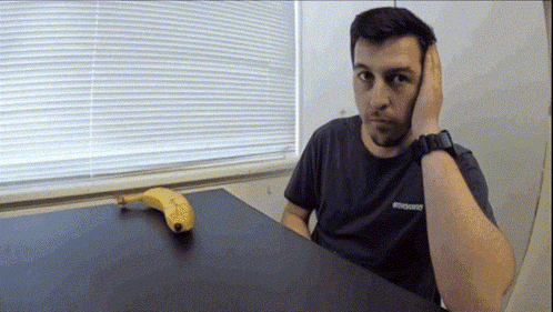a man wearing a black shirt that says brooklyn sits at a table with a banana
