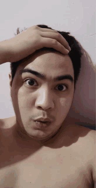 a shirtless man holds his hand to his head and looks surprised