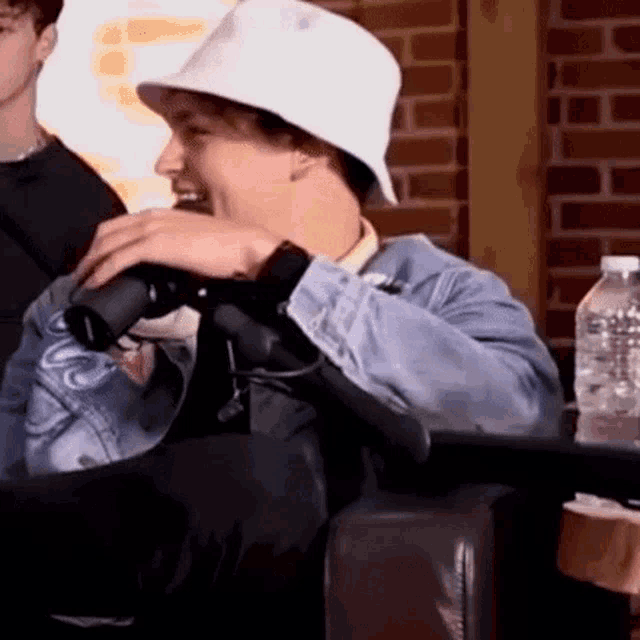 a man wearing a white hat and a denim jacket is sitting in a chair .