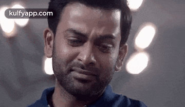 a man with a beard is crying with his eyes closed while wearing a blue shirt .
